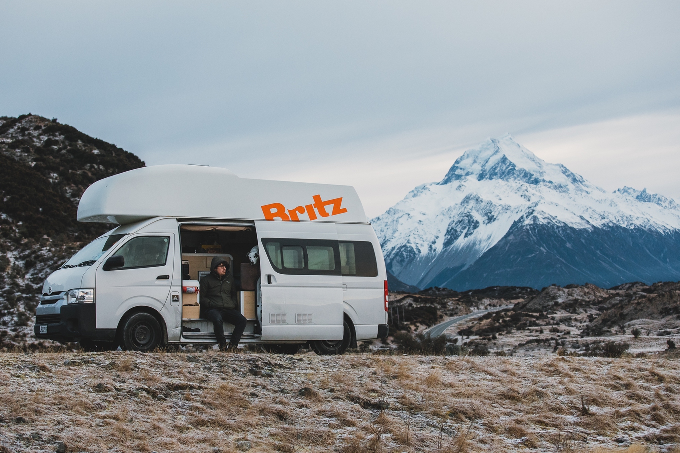 It's easy to stop and appreciate the scenery when you're travelling in a campervan A man on a roadtrip holiday sits in a campervan in front of a mountain